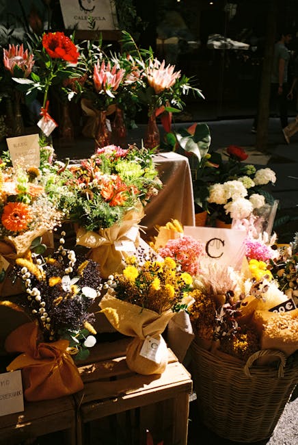 A vibrant display of fresh floral arrangements and bouquets at a flower shop, featuring a variety of flower types including red and pink proteas, white lilies, orange gerberas, yellow chrysanthemums,